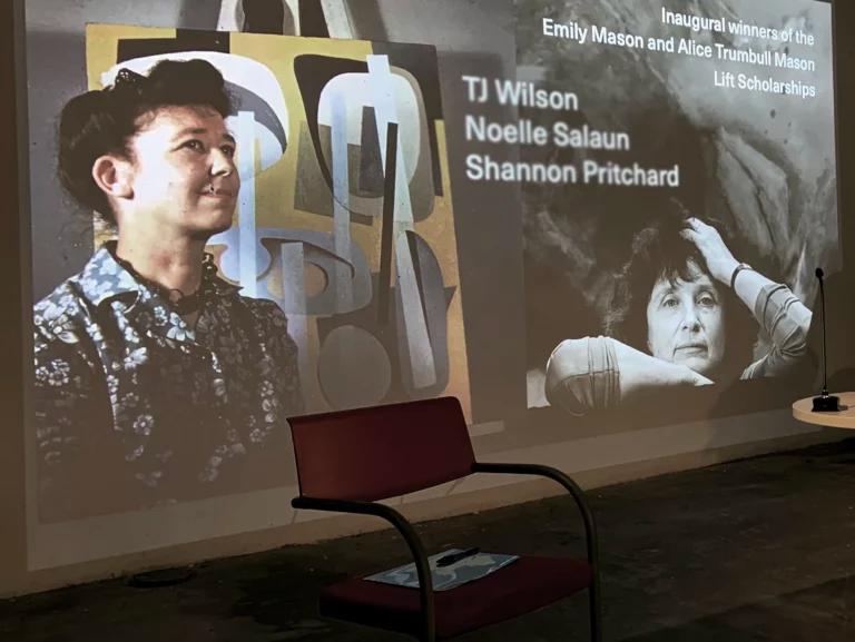 Photo of a setting with a projected image showing photos of two women with their artwork overlaid with text announcing scholarships.